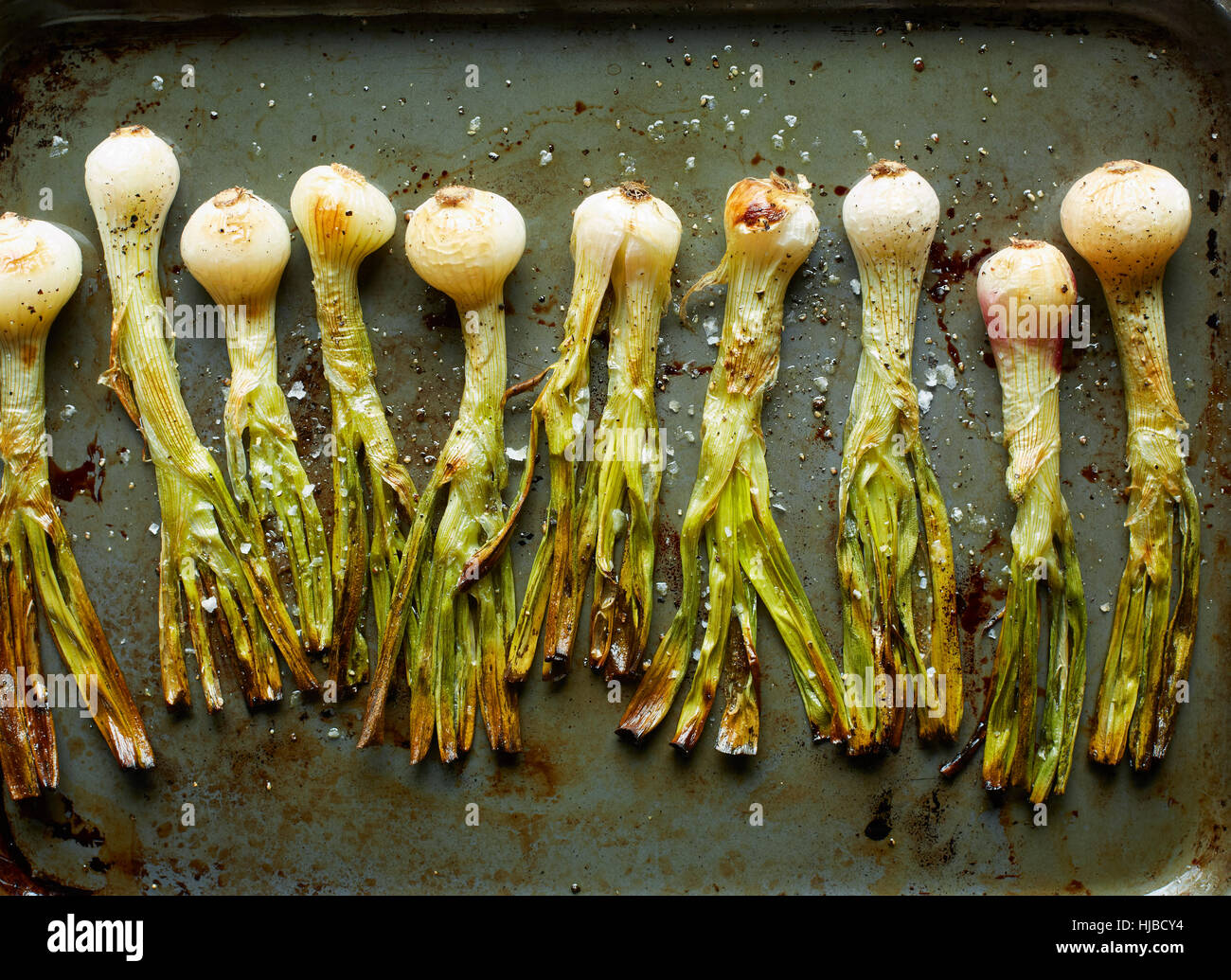 Overhead view of roasted whole spring onions in roasting tin Stock Photo