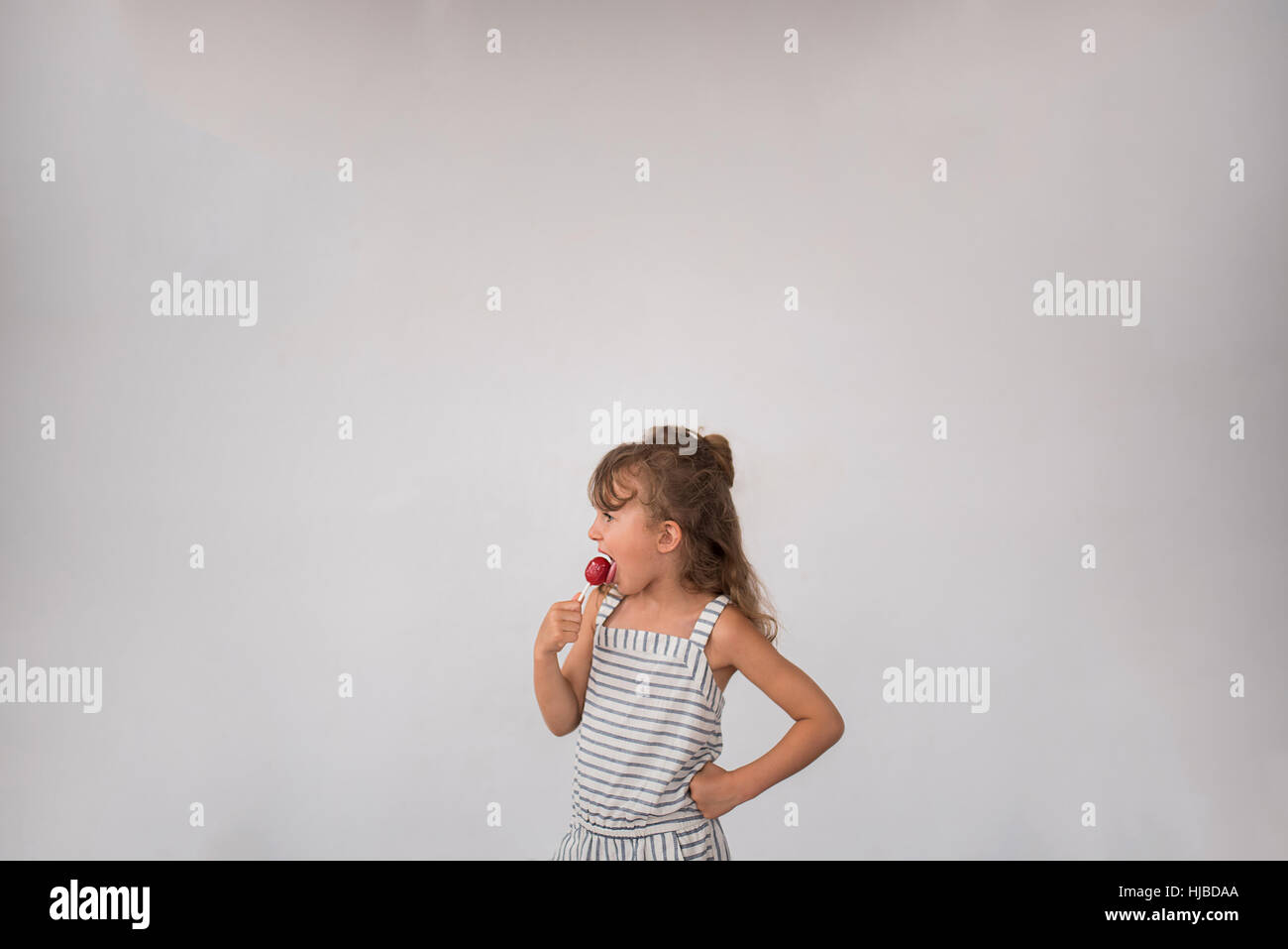 Little girl licking lollipop against white background Stock Photo