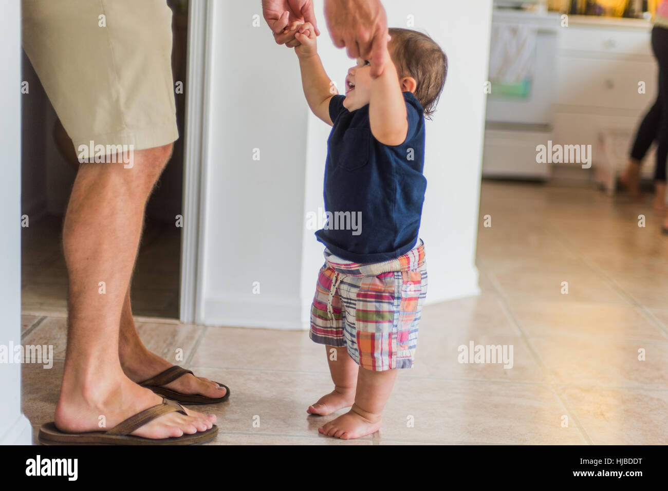 Father holding hands of toddler, guiding him to walk Stock Photo