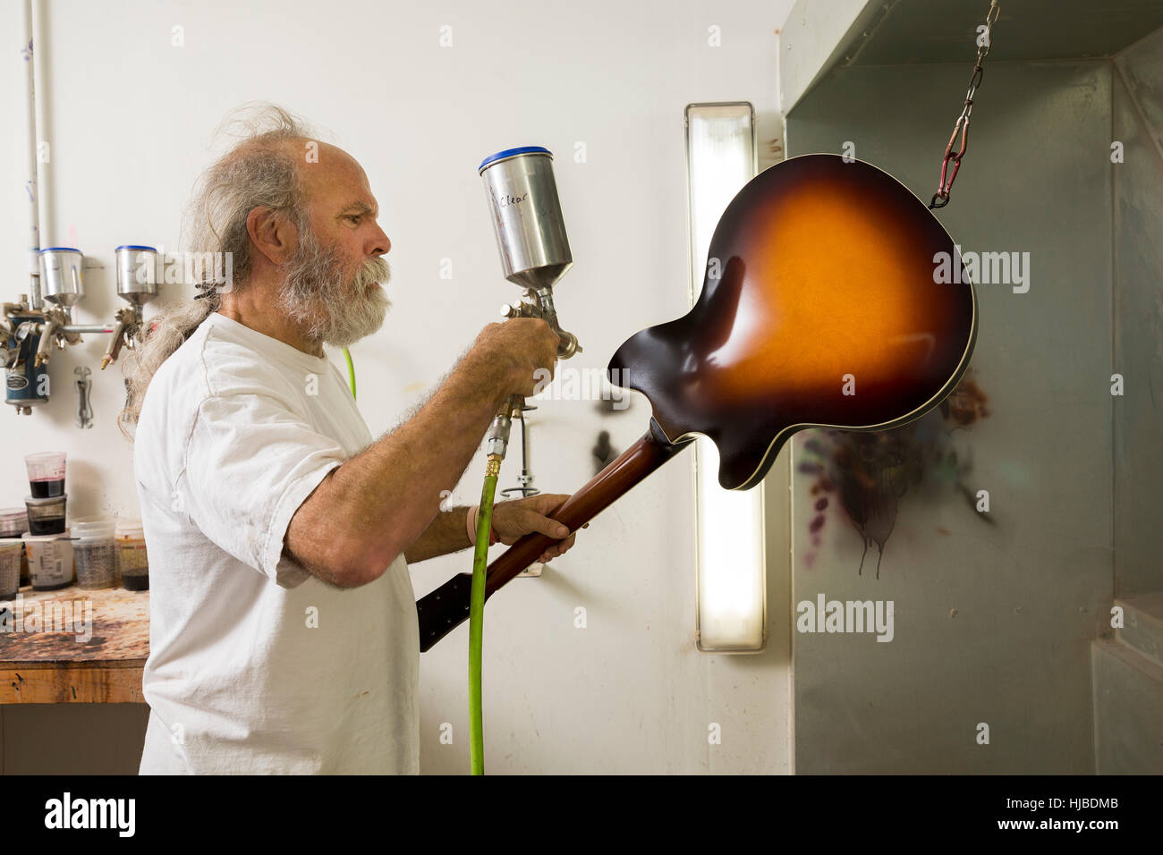 Guitar maker in workshop using spray gun to varnish guitar Stock