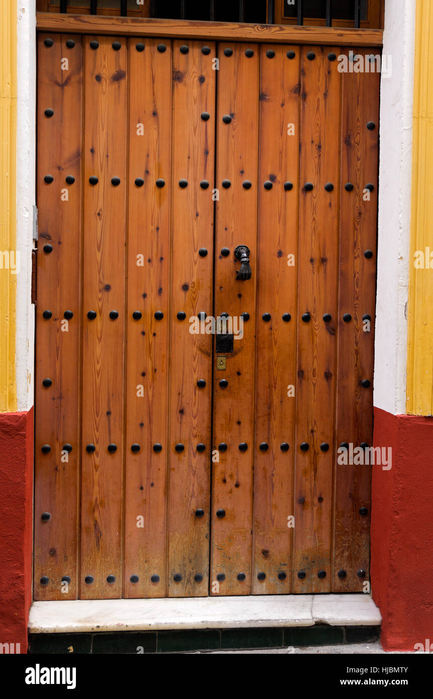Door made of wooden boards, held by large decorative brass bolts.  Metal door knocker in shape of closed fist. Stock Photo