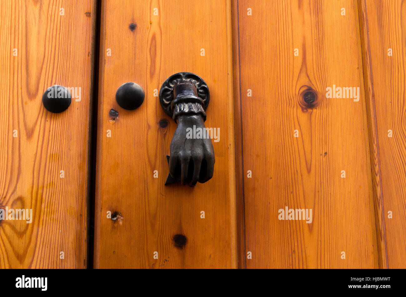 Close up of door made of wooden boards, held by large decorative brass bolts.  Metal door knocker in shape of closed fist. Stock Photo
