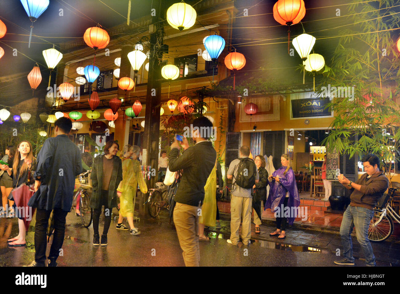 Global Tourists take Photos and Selfies on Hoi An Street with Colorful Orange, Blue, Yellow Lanterns above in Shopping District Stock Photo