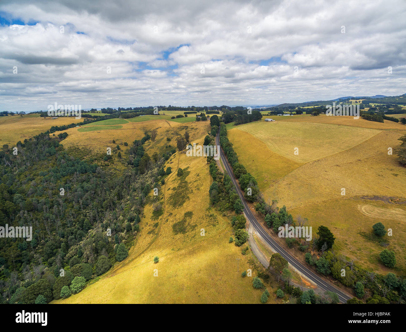 Aerial landscape of rural road among yellow rolling hills in Australian countryside Stock Photo