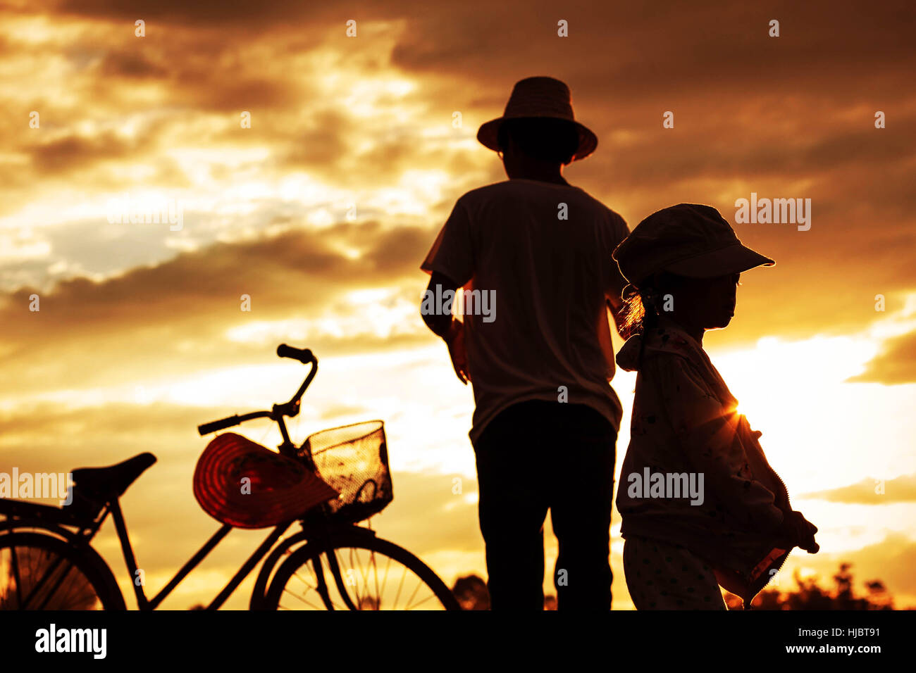 Father and son standing back with silhouettes at sunset. Stock Photo