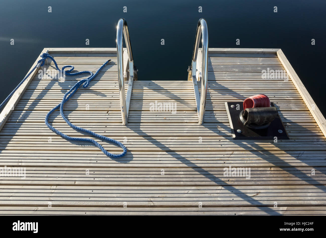 Small floating wooden marina pier with ropes and metal railings Stock Photo