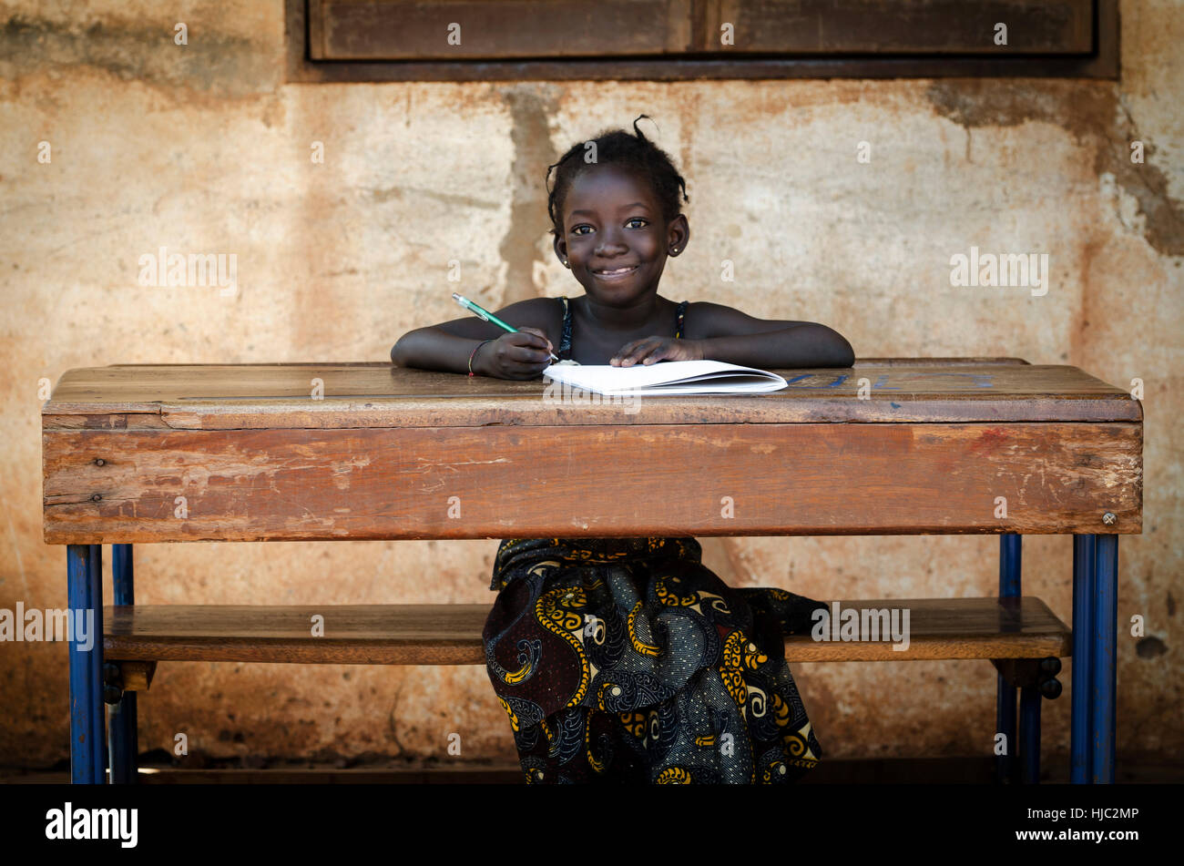 School Background: Proud African Schoolgirl Sitting In Her Desk Smiling Stock Photo