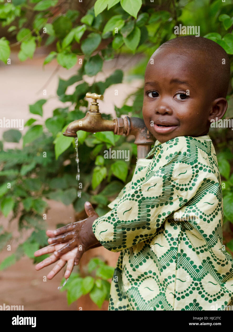 Young African school boy holding hands under a tap. Water scarcity problems concern the inadequate access to safe drinking water. 1 billion people in  Stock Photo