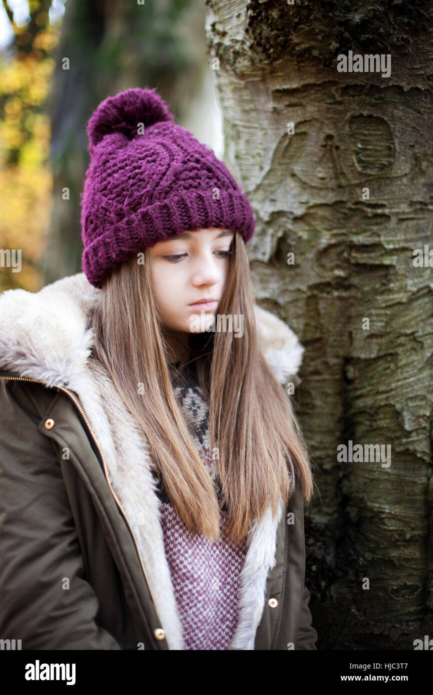 Teenage girl wearing a woolen hat standing beside a tree Stock Photo