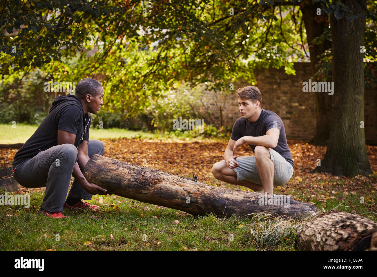 Personal trainer showing young man how to lift tree trunk in park Stock ...