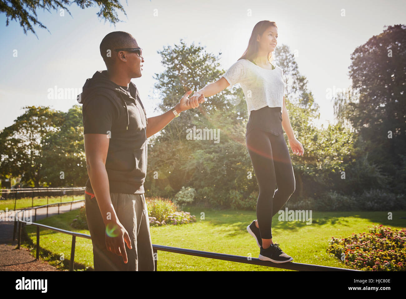 Woman holding hands with  personal trainer walking on park fence Stock Photo