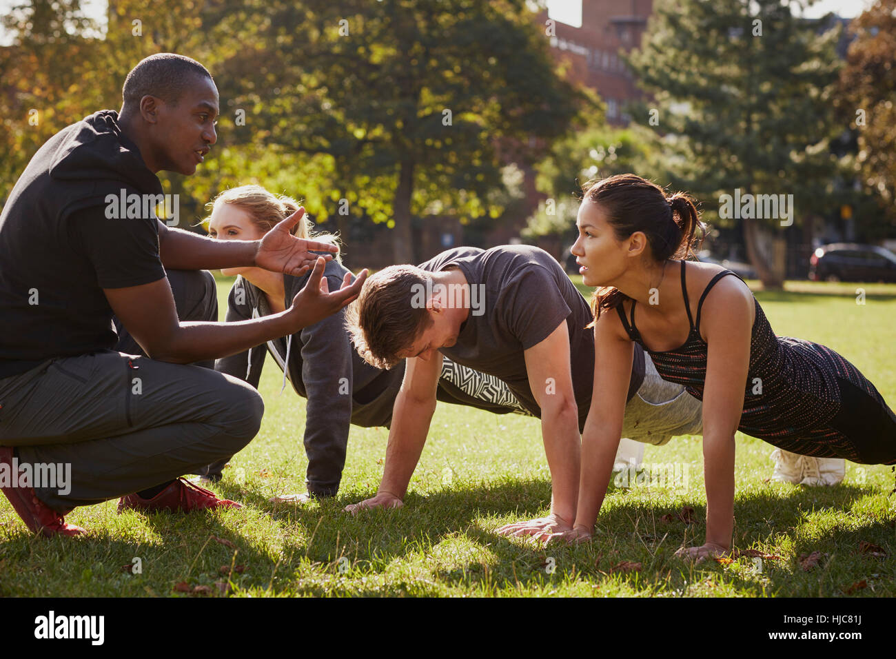 Personal Trainer Instructing Man And Women Doing Push Ups In Park Stock