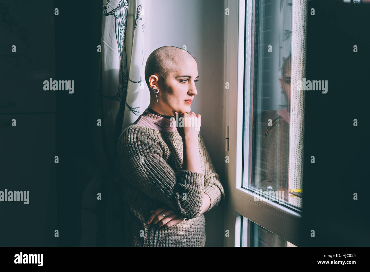 Portrait of young woman with shaved head gazing through window Stock Photo