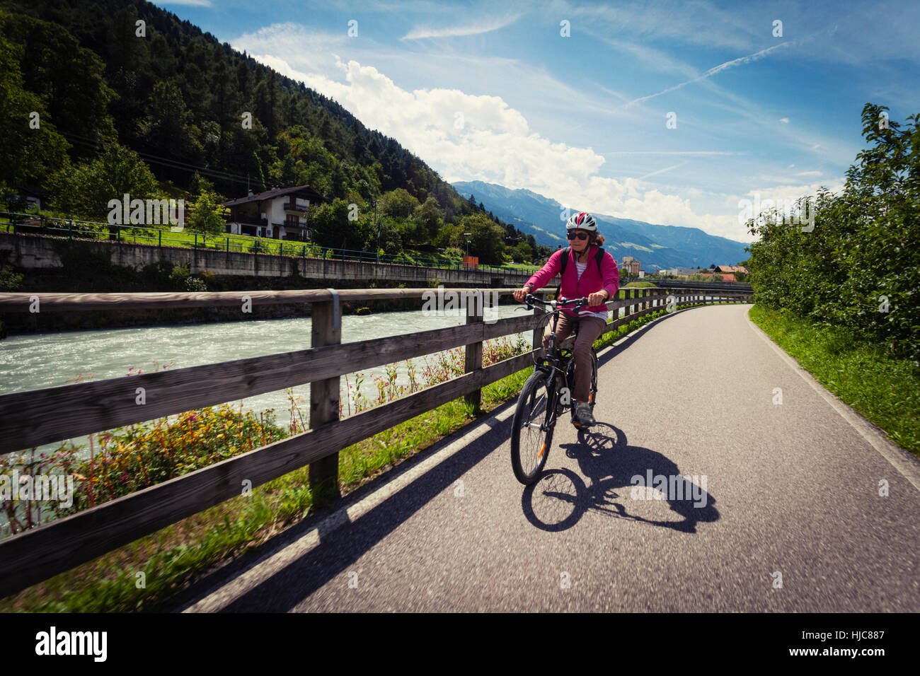 Female cyclist cycling along path by river in Vinschgau Valley, South Tyrol, Italy Stock Photo