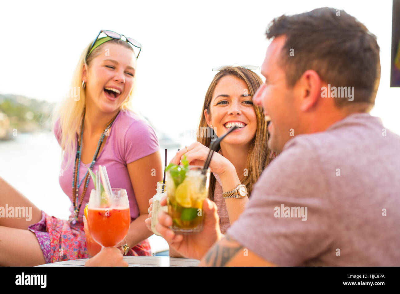 Three adult friends laughing over cocktails at waterfront restaurant, Majorca, Spain Stock Photo