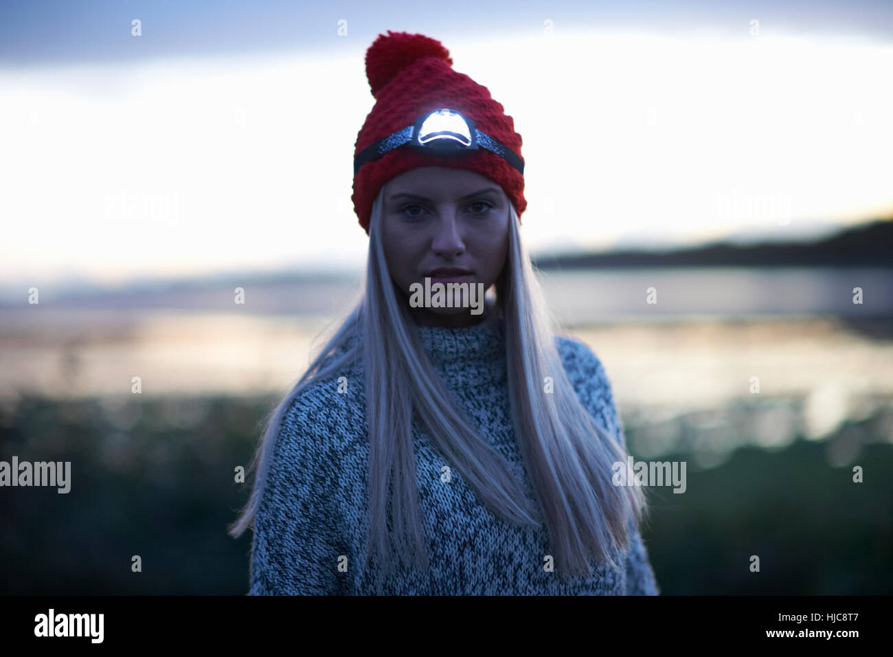 Portrait of young woman with head torch by sea at dusk Stock Photo