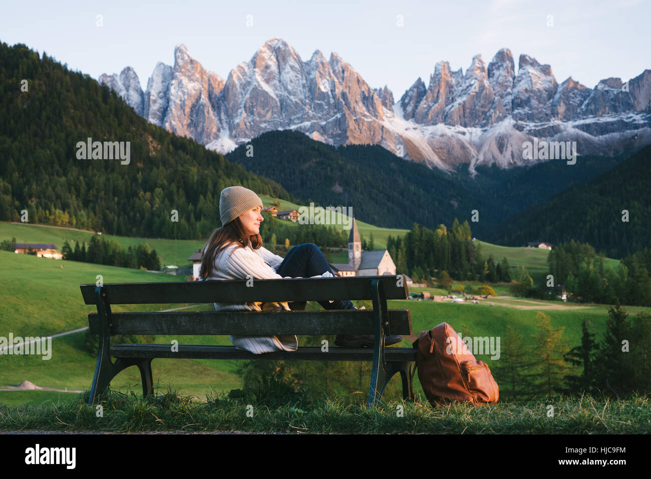 Woman relaxing on park bench, Santa Maddalena, Dolomite Alps, Val di Funes (Funes Valley), South Tyrol, Italy Stock Photo