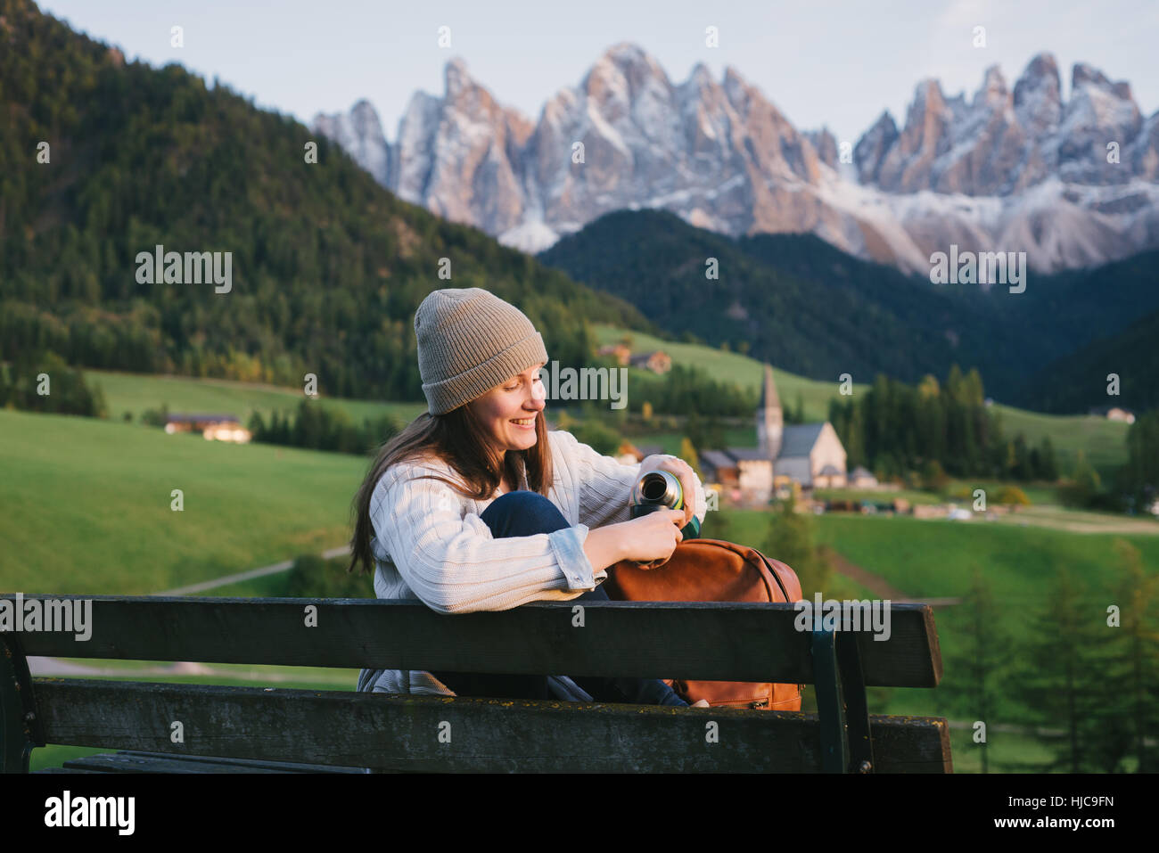 Woman relaxing on park bench, Santa Maddalena, Dolomite Alps, Val di Funes (Funes Valley), South Tyrol, Italy Stock Photo