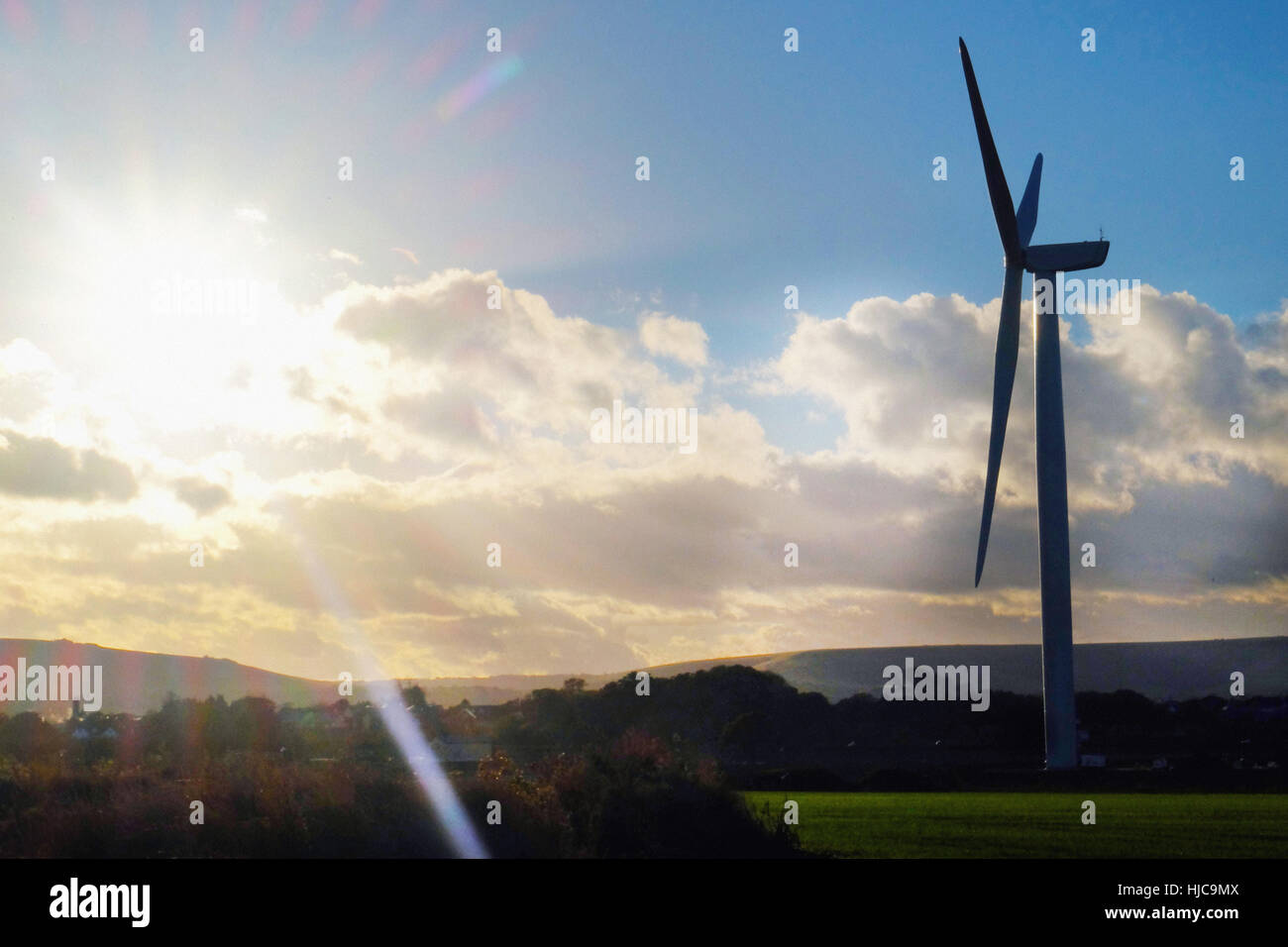 Sunlit silhouetted wind turbine in rural landscape Stock Photo