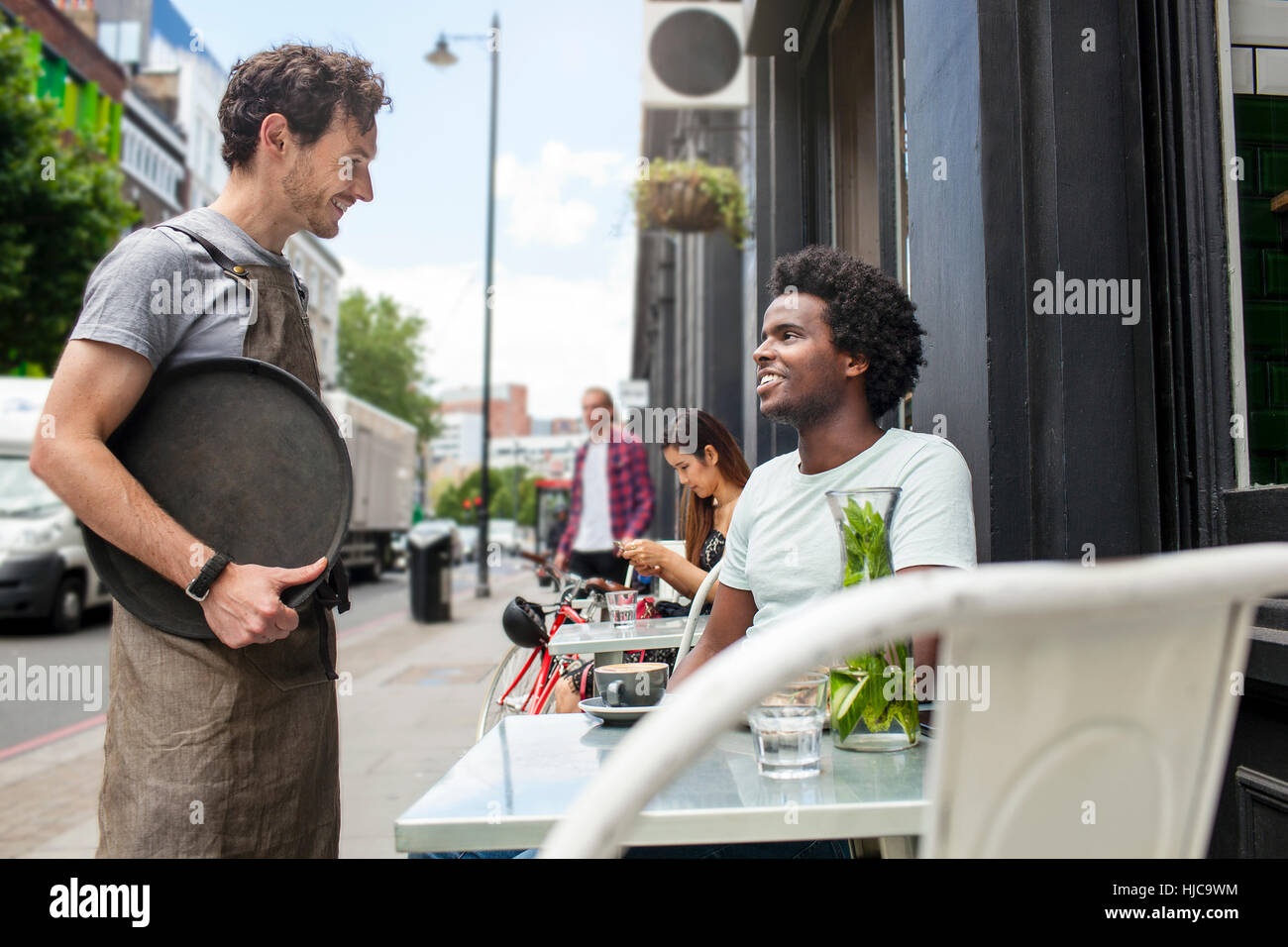 Waiter serving young man at city sidewalk cafe Stock Photo