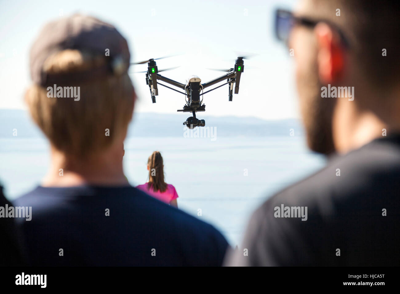 Rear view of man and woman looking at drone flying mid air over coast, Split, Dalmatia, Croatia Stock Photo