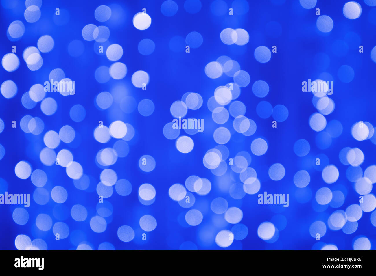 Blurry bokeh bright light from tiny lamps on blue and violet screen background at night Stock Photo