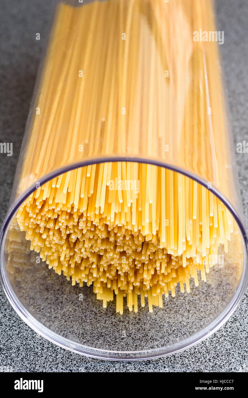 Dry and uncooked spaghetti inside transparent plastic canister. Stock Photo