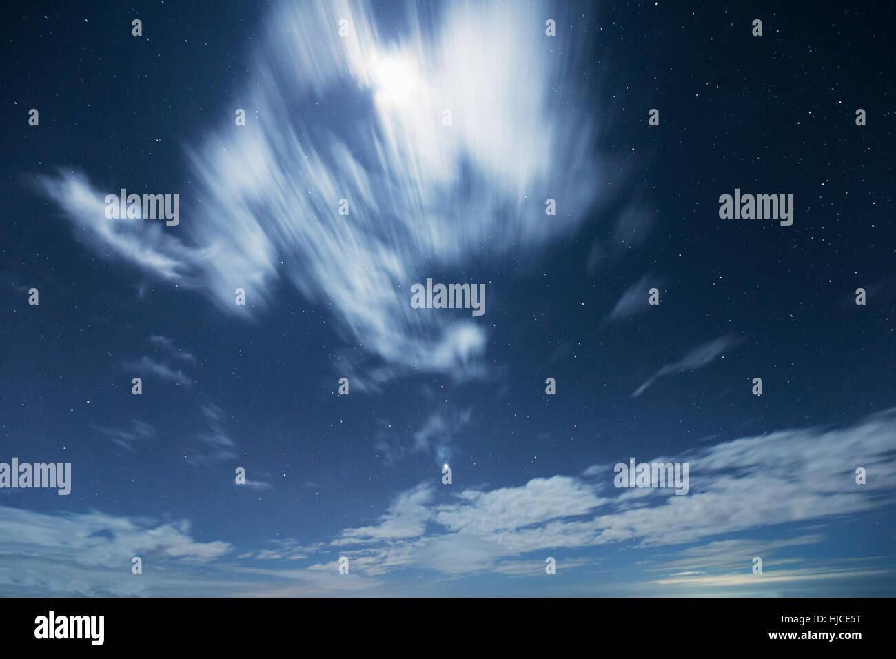 Night scene of graduated dark blue sky with stars and moving cloud cover light from moon in winter season. Stock Photo