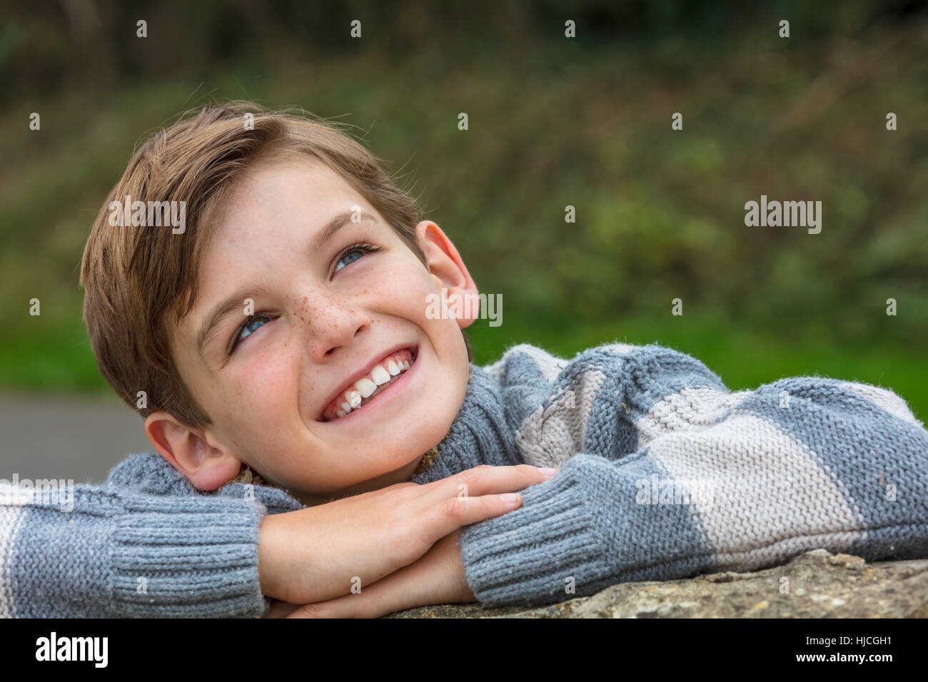 Young happy laughing male boy blond child outside leaning on his hands and looking up in autumn fall sunshine Stock Photo