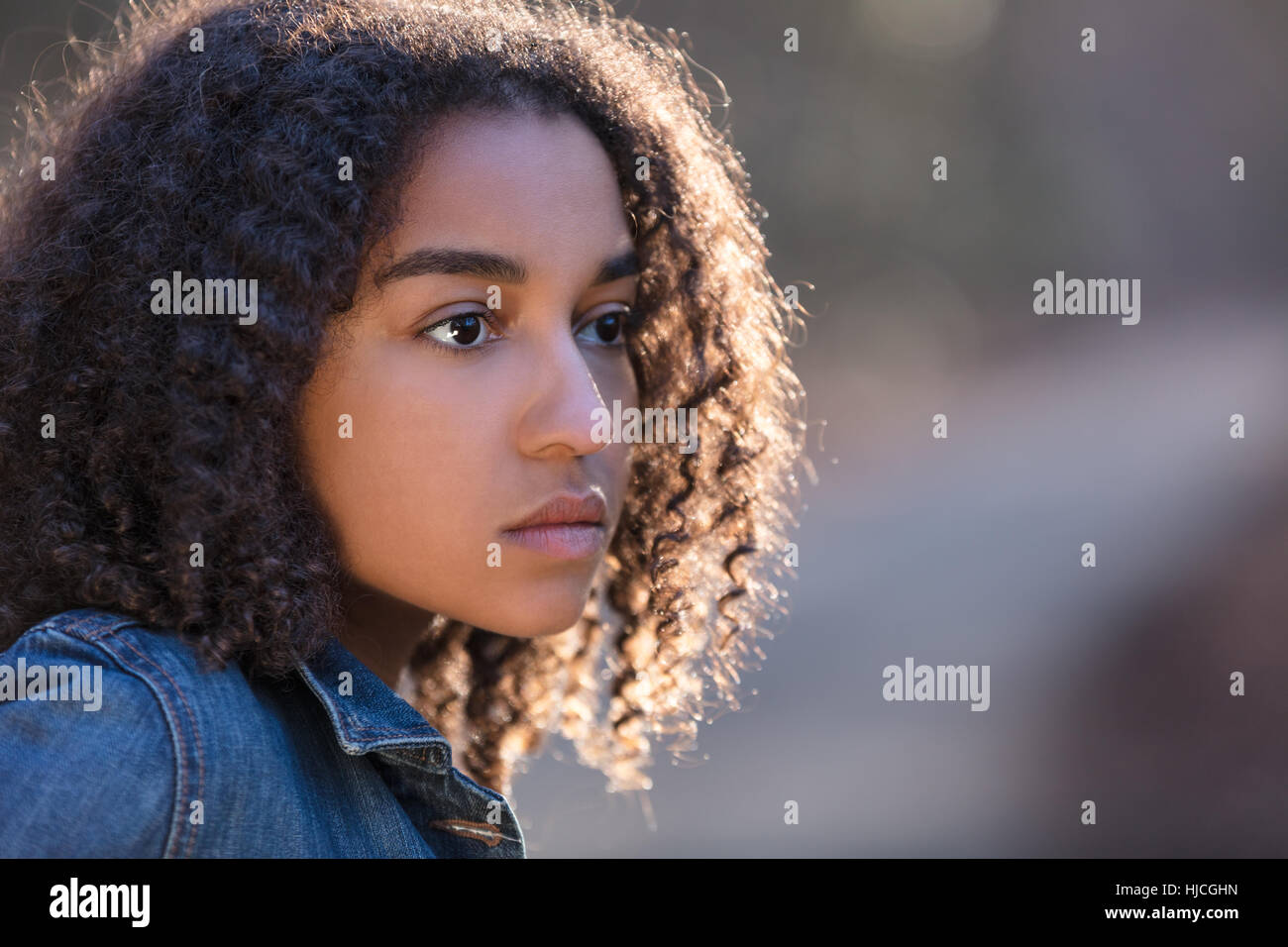 Beautiful mixed race African American girl teenager female young woman outside by a road looking sad depressed or thoughtful Stock Photo