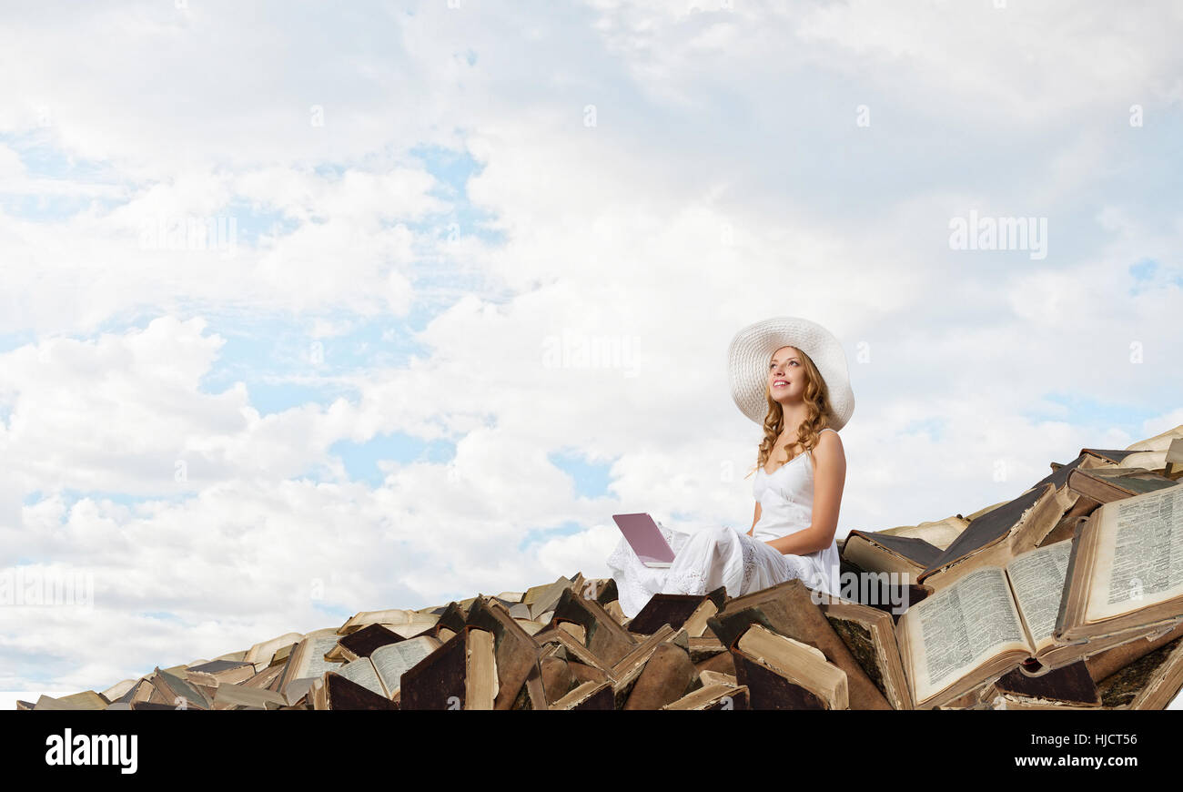 Young lady sitting on pile of books with laptop Stock Photo - Alamy