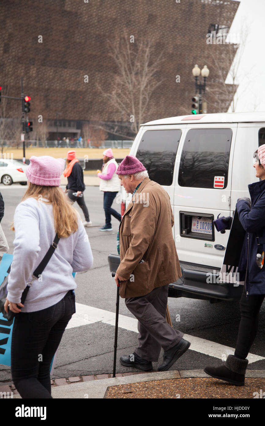 Washington, USA. January 21st, 2017. Women's March on Washington, DC: Older man with a walking cane donning a pink hat crossing Constitution Avenue with the new African American Museum in the background to reach the rally site to protest President Trump's positions on women's and other human rights. Credit: Dasha Rosato/Alamy Live News Stock Photo