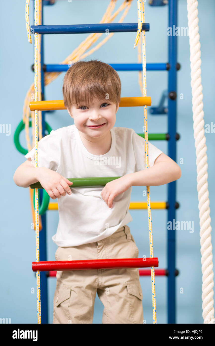 Little child playing sports at sport center. Kid boy standing on a rope ladder. Stock Photo