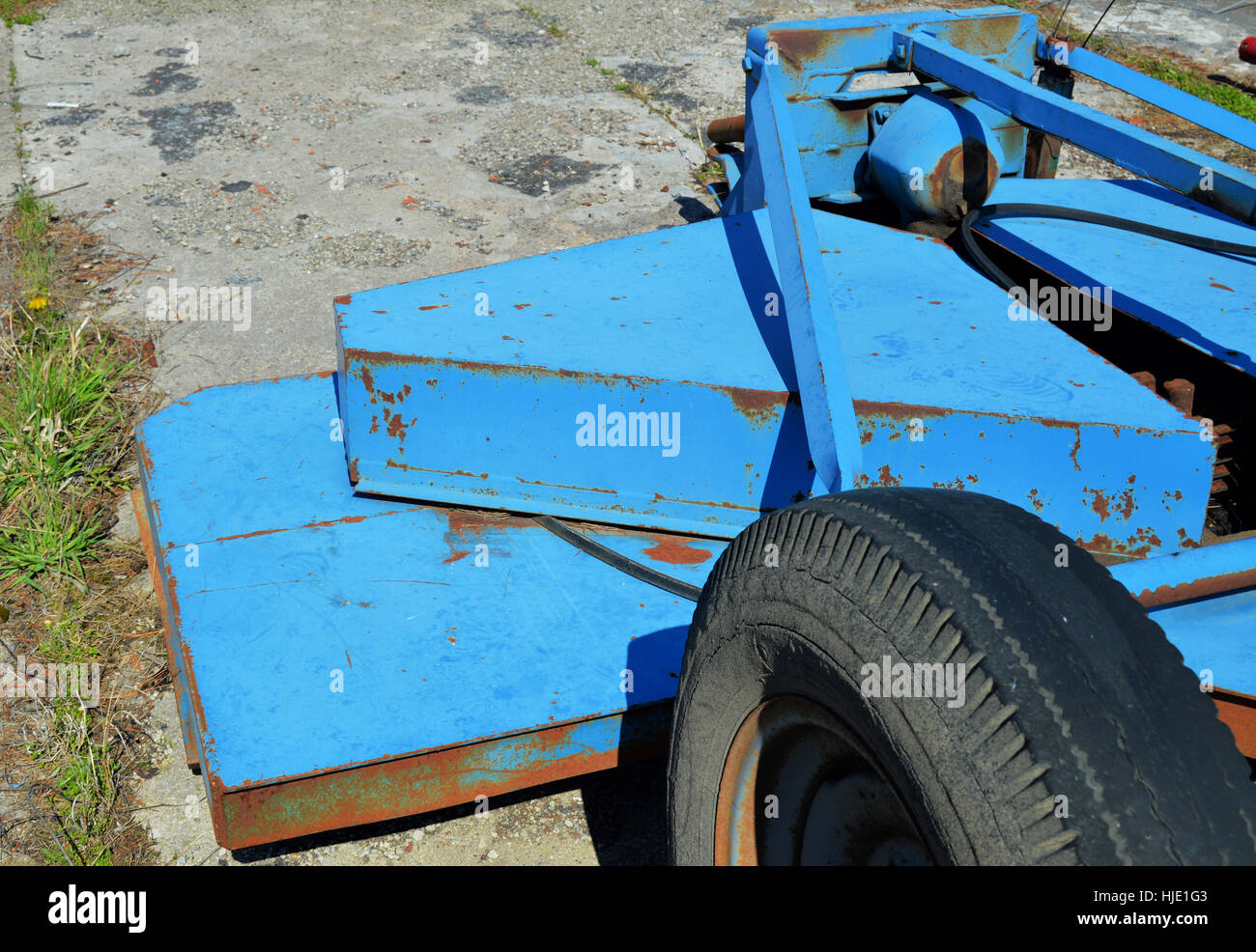 A blue industrial lawn mower sitting deserted on  broken concrete and weeds. Stock Photo