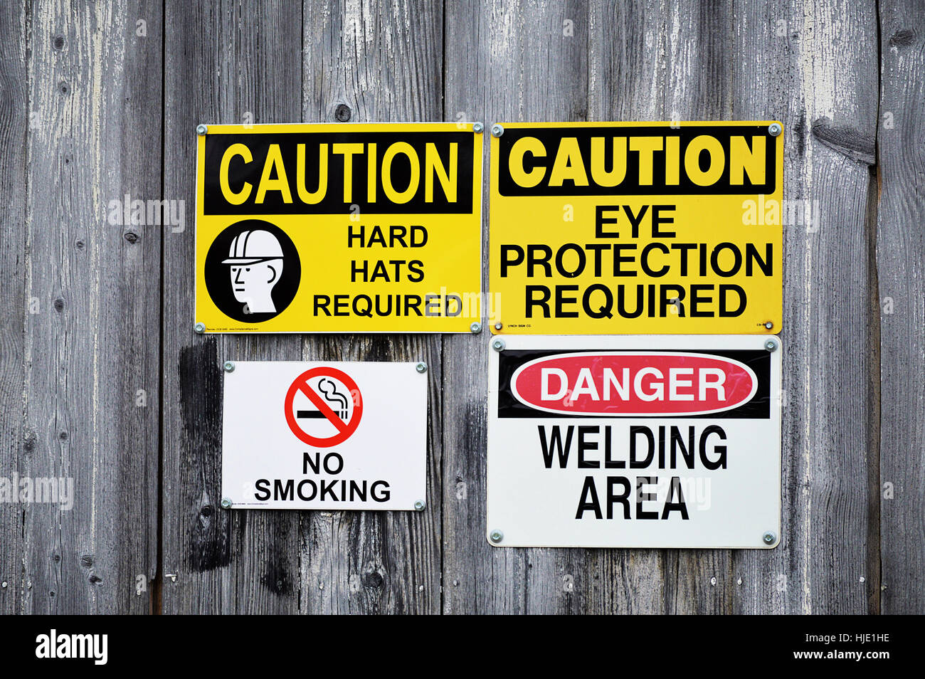A group of hard hat, eye protection,welding area, and no smoking signs on a wood wall. Stock Photo