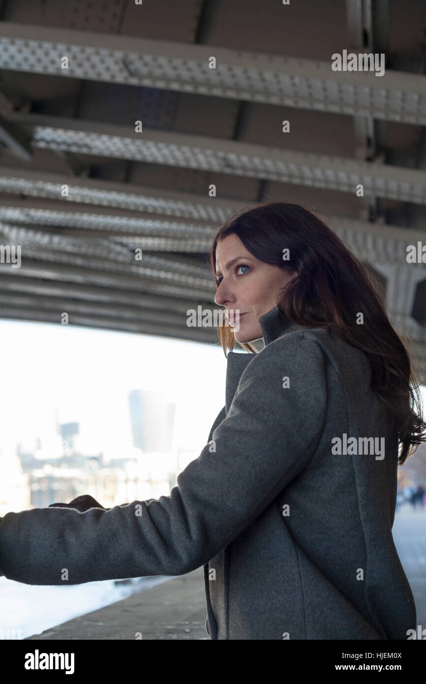 Attractive dark haired woman looks out from under a bridge in a tense and anxious urban setting Stock Photo