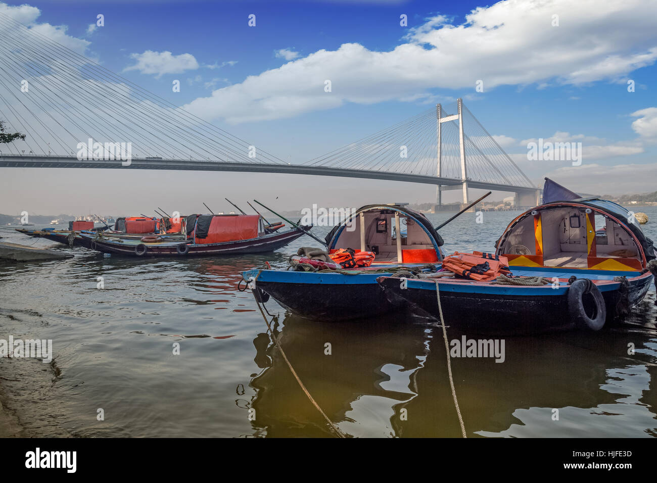 Scenic landscape with wooden boats lined up at the Hooghly river bank overlooking the famous Vidyasagar setu bridge. Stock Photo