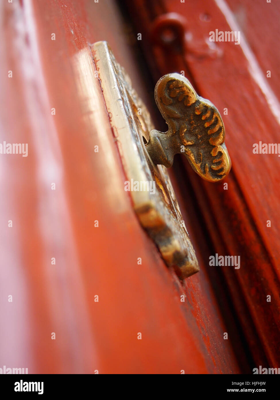 Extreme closeup of a fancy antique brass doorknob on an old red door. Stock Photo