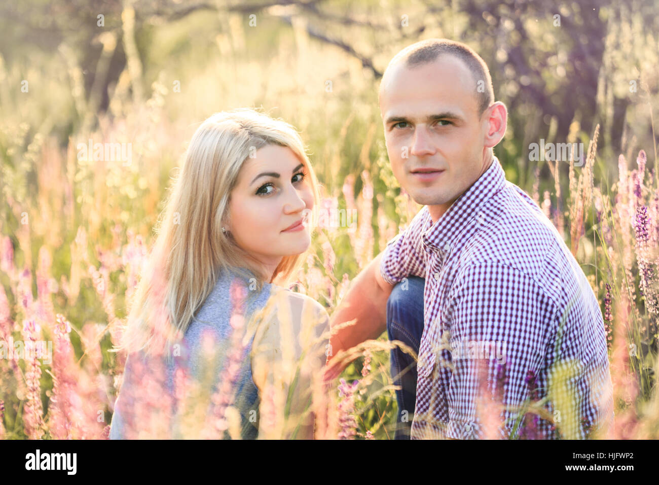 A handsome man and an attractive woman sitting on nature in flowers ...