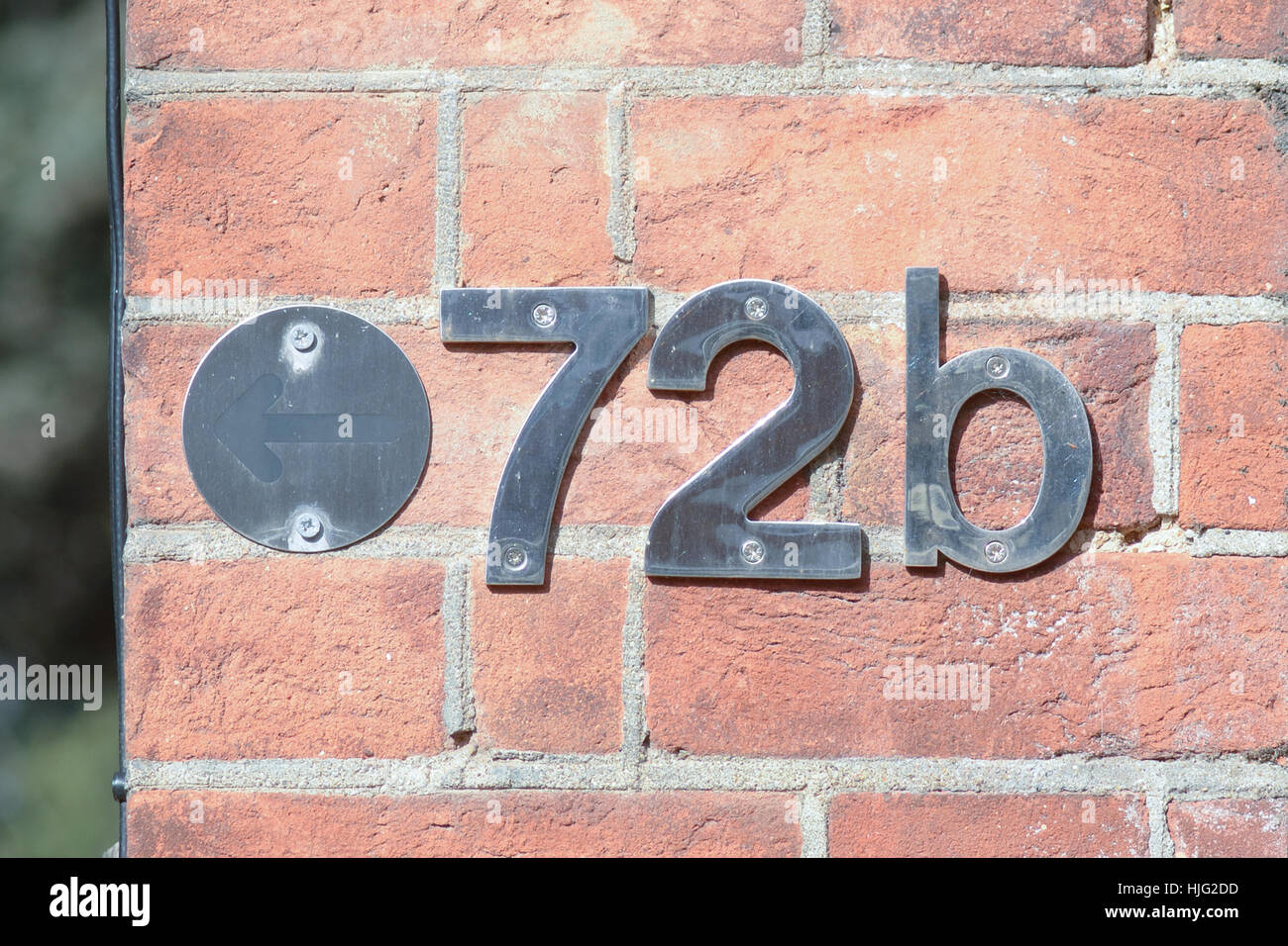 House number 72B sign with metal numbers screwed to red brick wall