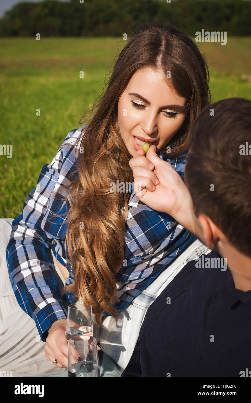 man feeding grapes woman at a picnic on the green grass background