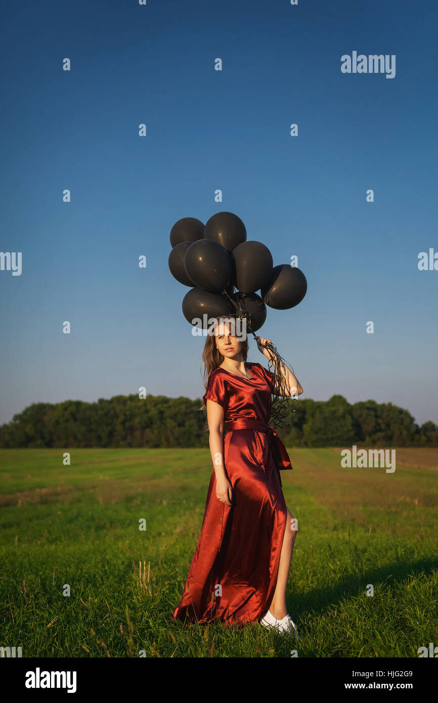 girl in red dress with black balloons standing in a field on the grass
