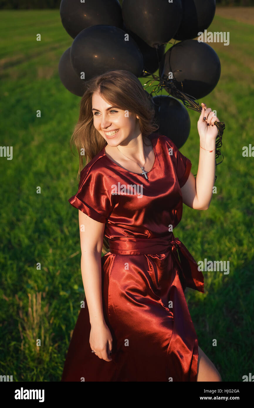 beautiful woman in a red dress with black balloons on green grass background Stock Photo