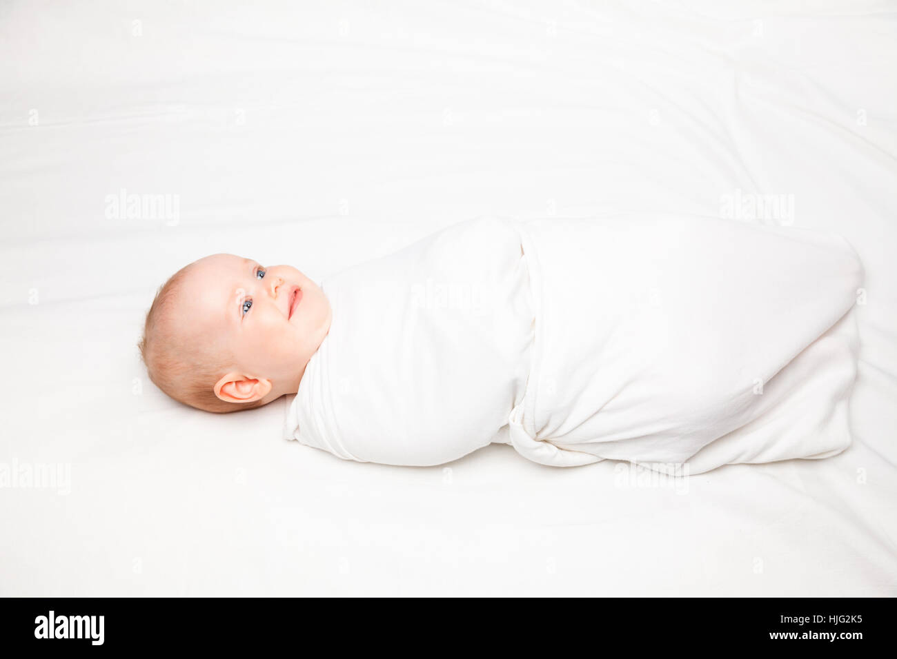 Three month baby girl swaddled in white blanket laying on a bed