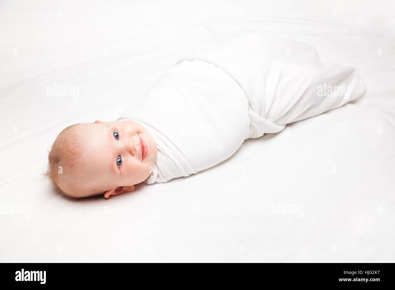 Three month baby girl swaddled in white blanket laying on a bed