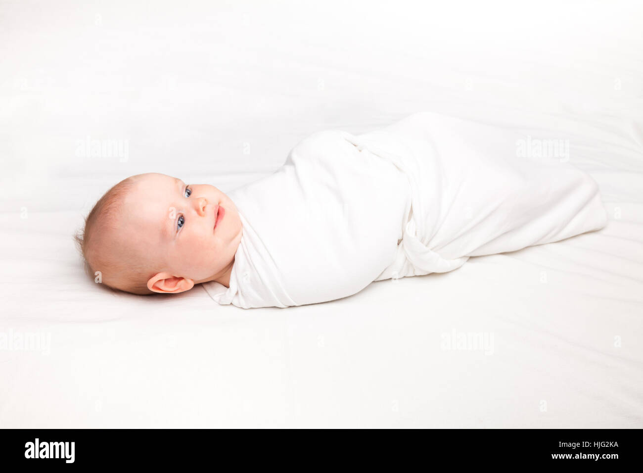 Three month baby girl swaddled in white blanket laying on a bed
