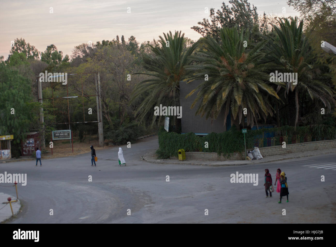 Street in Northern Ethiopia, Mekelle, with people in white robes and everyday clothing passing palm trees Stock Photo