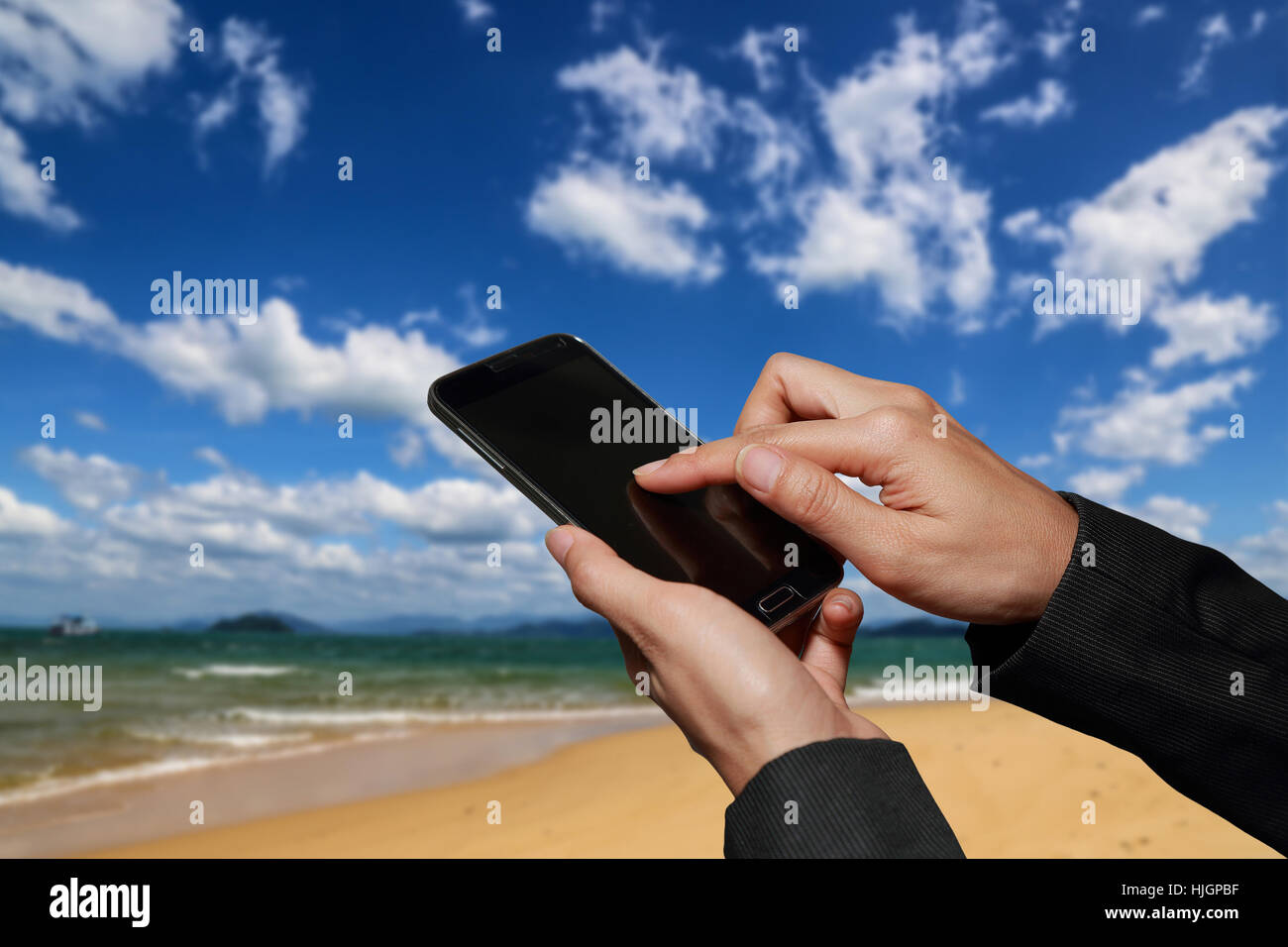 woman hand hold and touch screen smart phone, cellphone on blurred abstract blue and cloudy sky on the beach background. Stock Photo