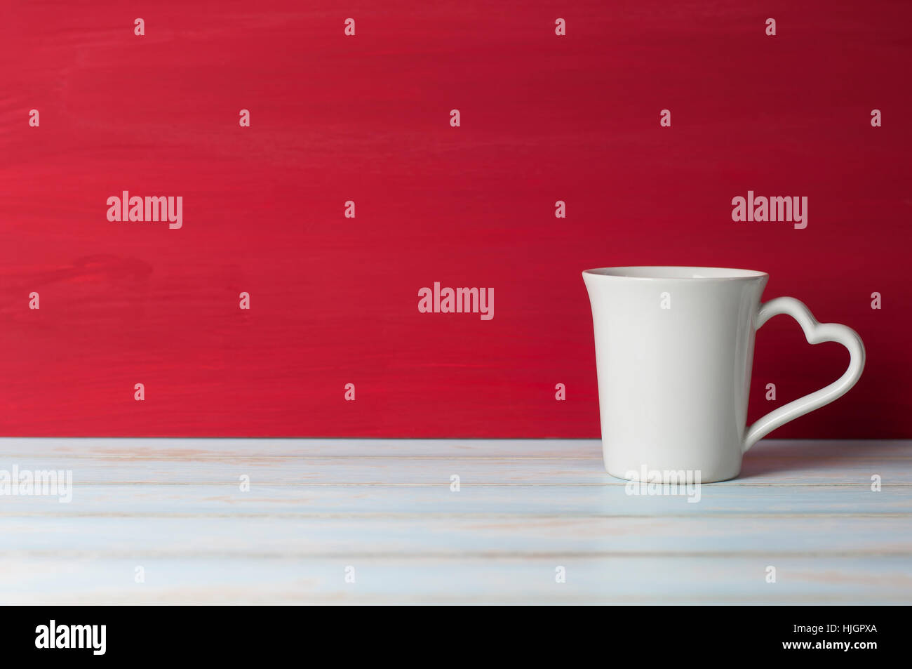 White mug with heart handle in front red grunge background on white table. Valentines concept. Stock Photo