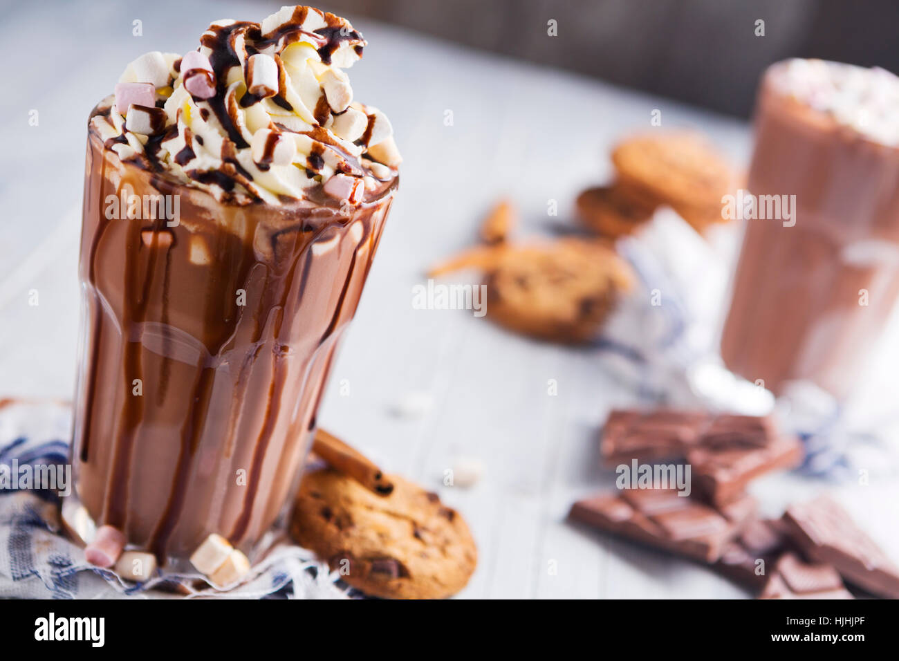 A messy glass with hot chocolate, whipped cream, marshmallows and chocolate chip cookies. Stock Photo